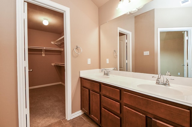 bathroom featuring tile patterned floors, double vanity, visible vents, a sink, and a walk in closet