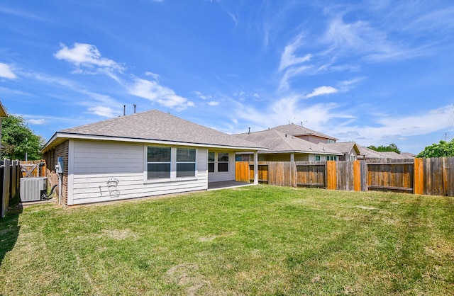 rear view of property with a lawn, a fenced backyard, central AC unit, and roof with shingles