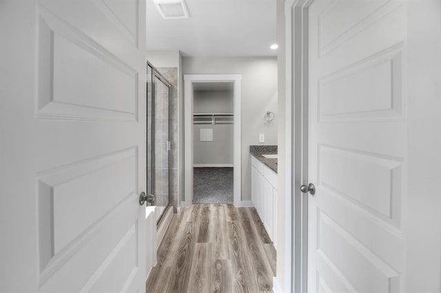 full bath featuring a shower stall, wood finished floors, a spacious closet, and visible vents