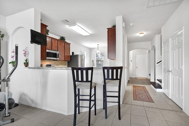 kitchen featuring a peninsula, light tile patterned flooring, visible vents, appliances with stainless steel finishes, and arched walkways