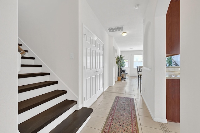 foyer with baseboards, stairway, light tile patterned flooring, visible vents, and arched walkways