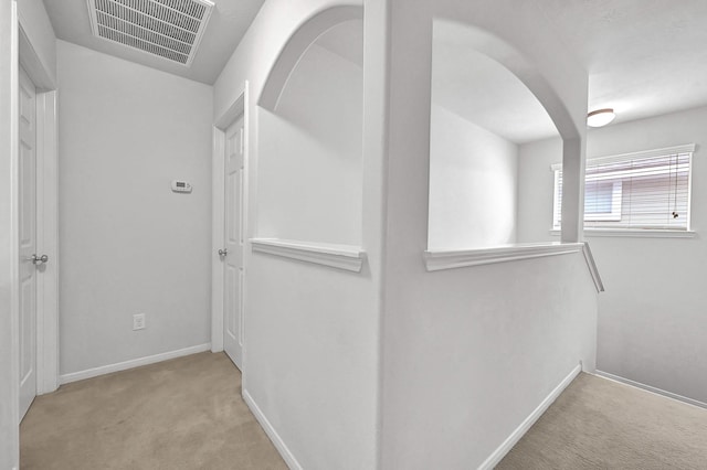 corridor featuring arched walkways, baseboards, visible vents, and carpet floors