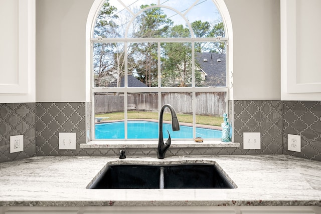 14102 Haynes Dr, Houston, TX 77069 - interior details featuring light stone counters, decorative backsplash, a sink, and white cabinetry