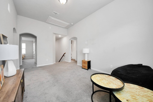 living area with baseboards, an upstairs landing, attic access, carpet floors, and arched walkways