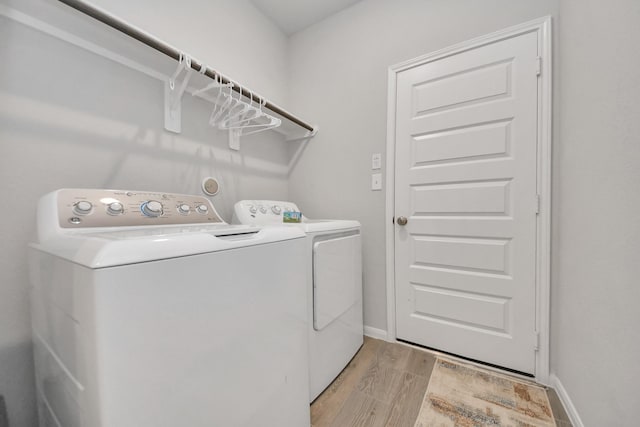 clothes washing area with baseboards, light wood-style floors, washer and dryer, and laundry area