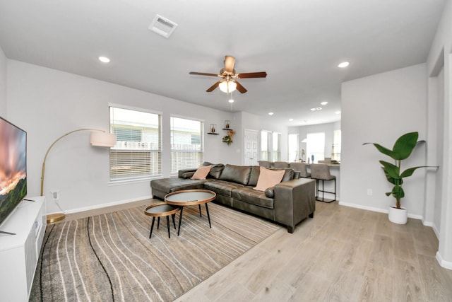 living area with light wood-style flooring, a ceiling fan, visible vents, and a wealth of natural light