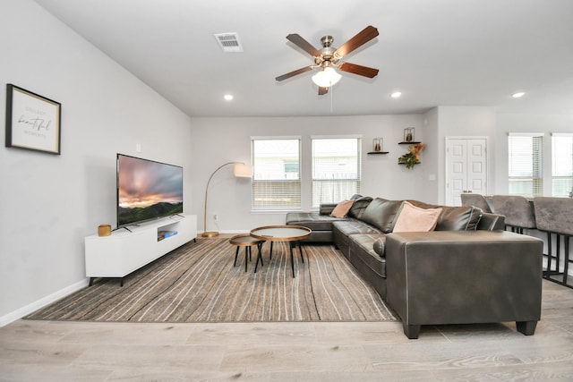 living area featuring visible vents, a wealth of natural light, a ceiling fan, and light wood-style floors