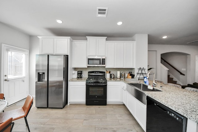 kitchen featuring visible vents, a sink, a peninsula, black appliances, and white cabinetry