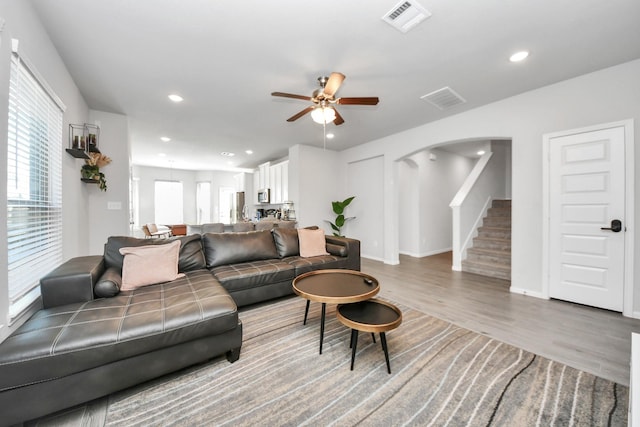 living area with arched walkways, stairway, visible vents, and a ceiling fan