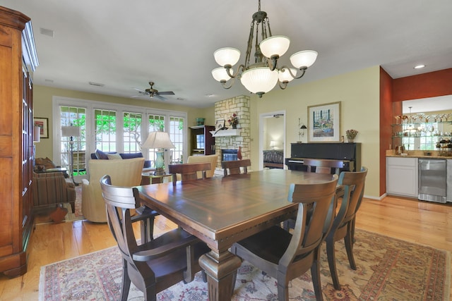 dining area featuring bar, light wood-type flooring, beverage cooler, and ceiling fan with notable chandelier