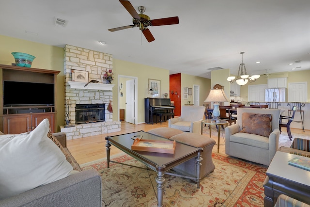 living area with a stone fireplace, recessed lighting, visible vents, ceiling fan with notable chandelier, and wood finished floors