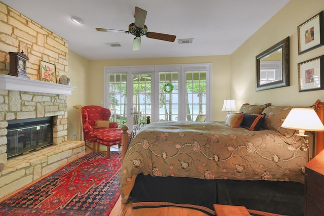 bedroom with access to exterior, ceiling fan, a stone fireplace, and visible vents