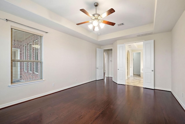unfurnished bedroom with visible vents, baseboards, a tray ceiling, and wood finished floors