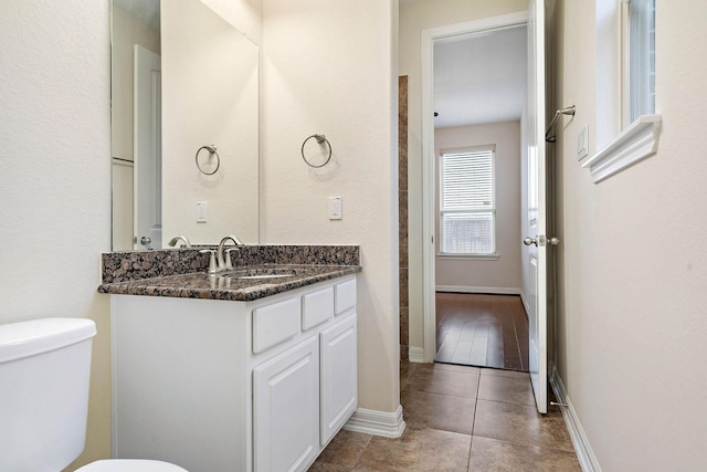 bathroom featuring tile patterned flooring, vanity, baseboards, and toilet