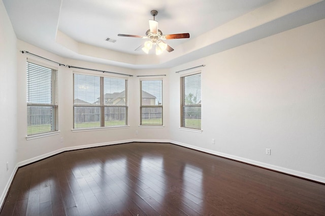 empty room with a raised ceiling, dark wood-style floors, baseboards, and a ceiling fan