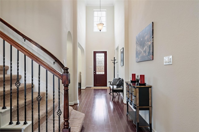 foyer with dark wood-type flooring, arched walkways, stairway, a high ceiling, and baseboards