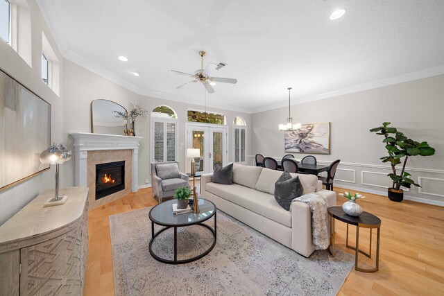 living room featuring ceiling fan with notable chandelier, plenty of natural light, a tiled fireplace, and wood finished floors