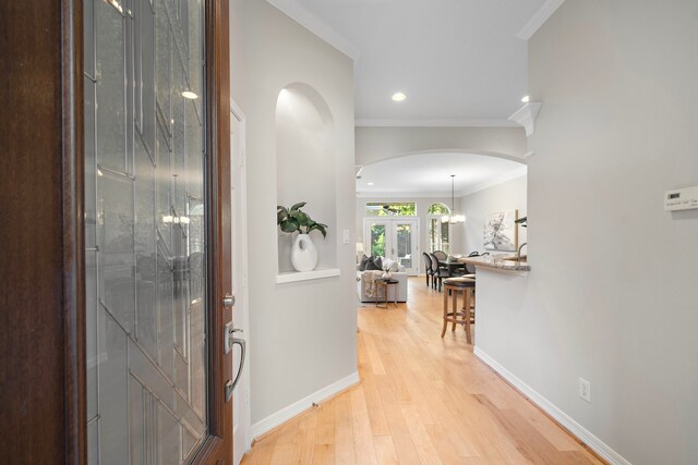 entryway featuring light wood-style flooring, arched walkways, baseboards, recessed lighting, and ornamental molding