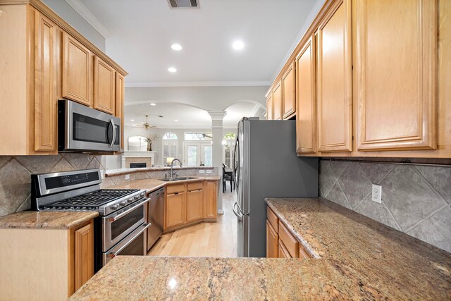 kitchen with a ceiling fan, arched walkways, appliances with stainless steel finishes, ornamental molding, and ornate columns