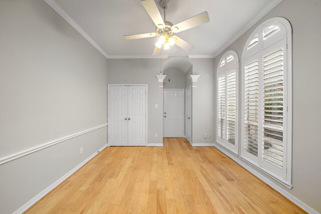 unfurnished bedroom with baseboards, light wood-style floors, a ceiling fan, a closet, and crown molding