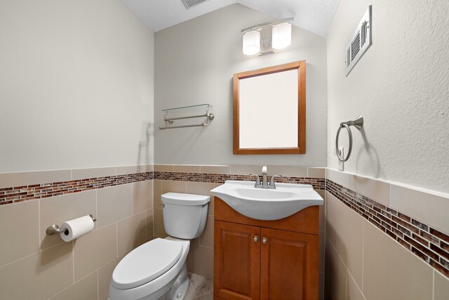 half bath with toilet, a wainscoted wall, visible vents, and tile walls