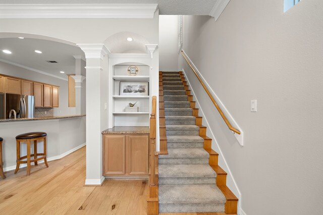 stairway with arched walkways, baseboards, recessed lighting, wood finished floors, and crown molding