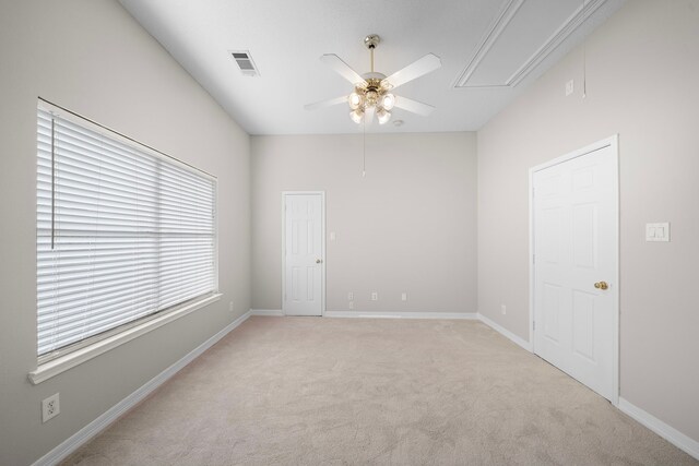 spare room featuring visible vents, baseboards, attic access, light colored carpet, and ceiling fan