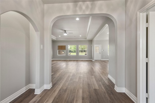 hallway with a tray ceiling, dark wood-style flooring, and baseboards