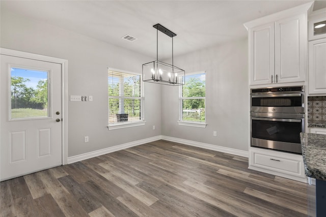 unfurnished dining area with a chandelier, dark wood-type flooring, baseboards, and visible vents