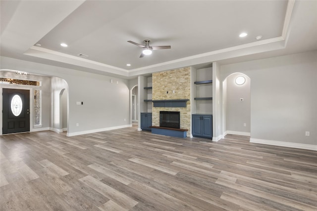 unfurnished living room with baseboards, arched walkways, a tray ceiling, and a ceiling fan