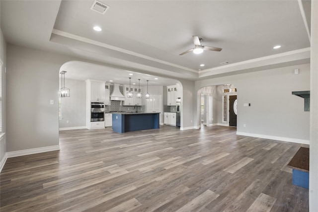unfurnished living room with a ceiling fan, visible vents, a tray ceiling, arched walkways, and a sink