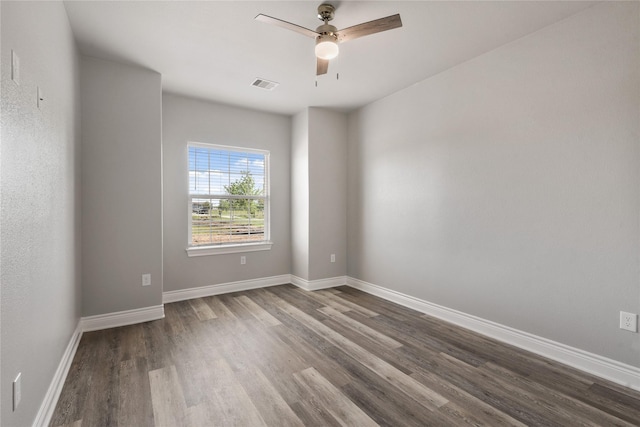 spare room with ceiling fan, visible vents, baseboards, and dark wood finished floors