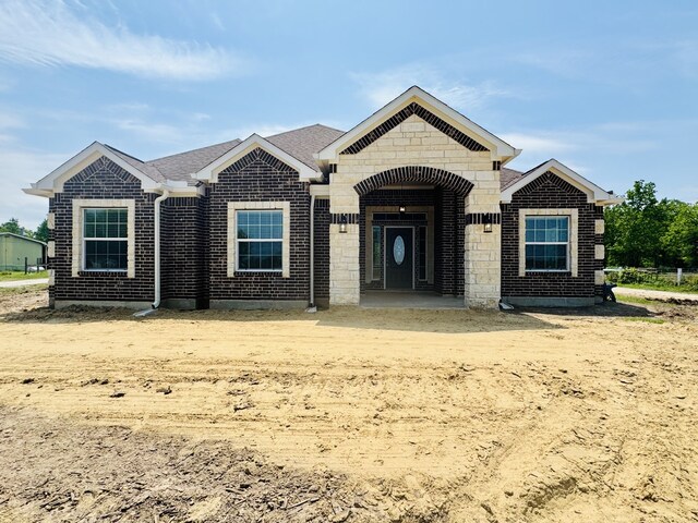 view of front facade featuring roof with shingles, stone siding, and brick siding
