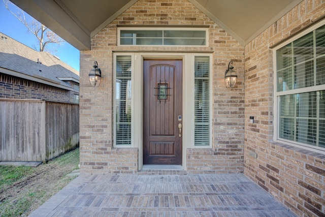 view of exterior entry with brick siding and fence