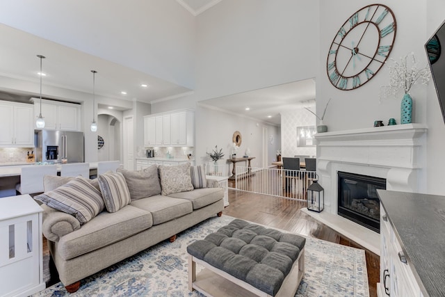 living room featuring crown molding, wood finished floors, recessed lighting, and arched walkways
