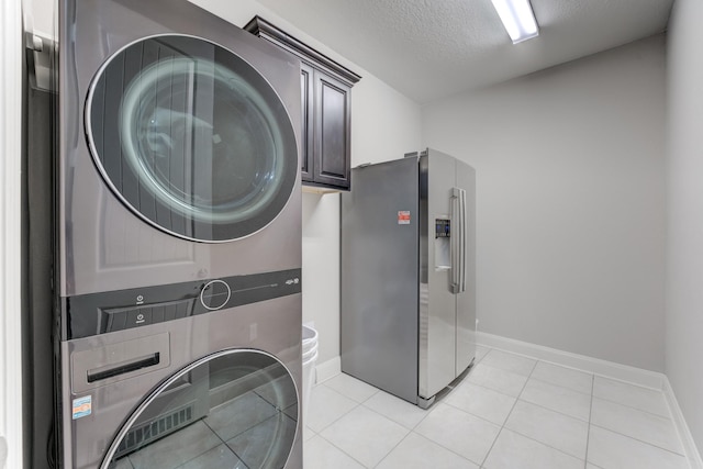 laundry area with light tile patterned floors, a textured ceiling, stacked washer / dryer, baseboards, and cabinet space
