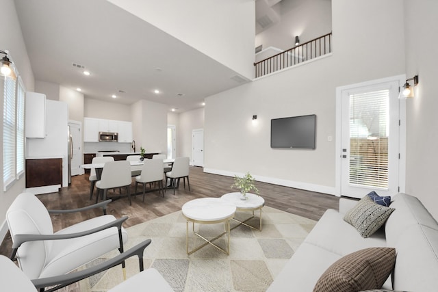 living area with visible vents, baseboards, a towering ceiling, and wood finished floors