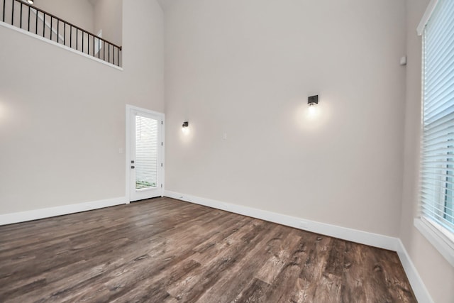spare room with baseboards, a towering ceiling, dark wood-type flooring, and plenty of natural light