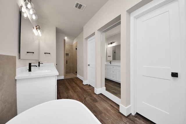 bathroom with two vanities, a freestanding bath, visible vents, wood finished floors, and a shower stall