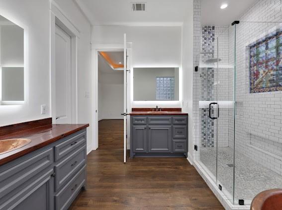 1408 W 23rd St, Houston, TX 77008 - bathroom with two vanities, visible vents, wood finished floors, a sink, and a stall shower