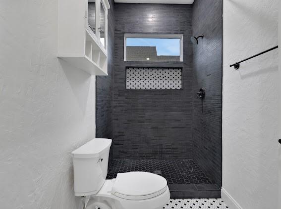 1408 W 23rd St, Houston, TX 77008 - bathroom with a tile shower, tile patterned floors, a textured wall, and toilet