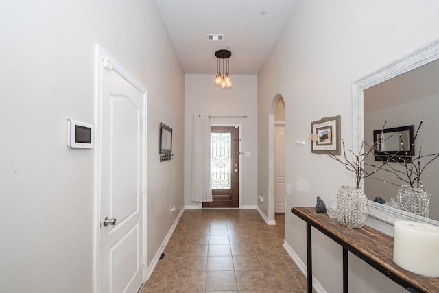 foyer featuring arched walkways, light tile patterned flooring, and baseboards