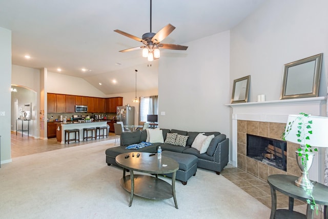 living room featuring a ceiling fan, a tile fireplace, light colored carpet, arched walkways, and recessed lighting