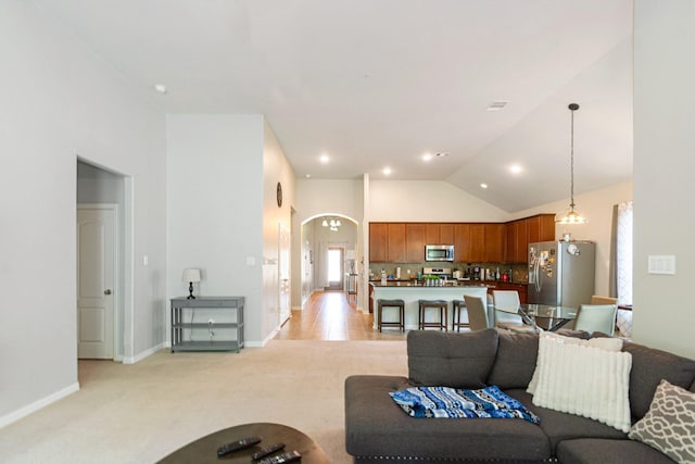 living area featuring arched walkways, high vaulted ceiling, light colored carpet, and baseboards