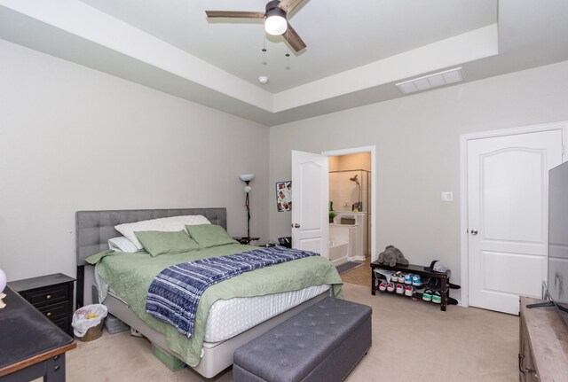 carpeted bedroom with a tray ceiling, a ceiling fan, and ensuite bath