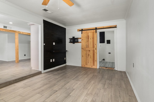 spare room with a barn door, wood finished floors, ceiling fan, and crown molding
