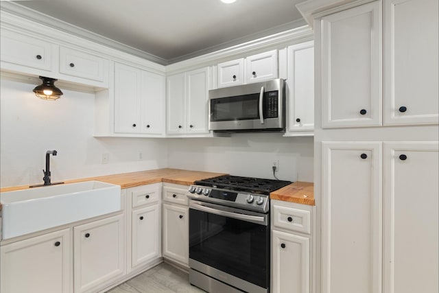 kitchen featuring a sink, butcher block countertops, appliances with stainless steel finishes, and white cabinetry
