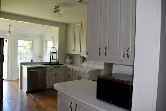 kitchen featuring light countertops, wood finished floors, stainless steel dishwasher, black microwave, and a peninsula