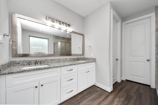 full bath featuring double vanity, a sink, a stall shower, and wood finished floors