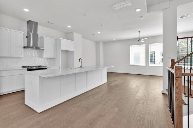 kitchen featuring visible vents, wall chimney exhaust hood, backsplash, light countertops, and white cabinets